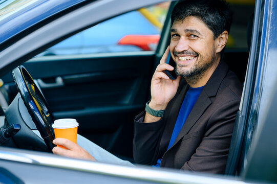 Smiling businessman talks on phone and holds coffee in his car