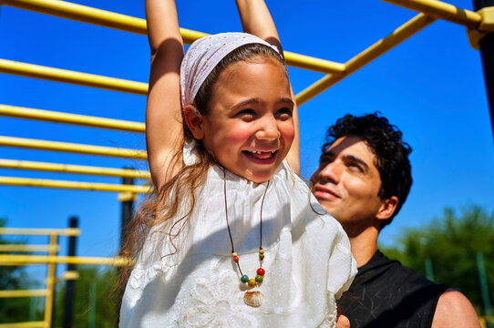 Smiling daughter hanging on monkey bars with father at playground