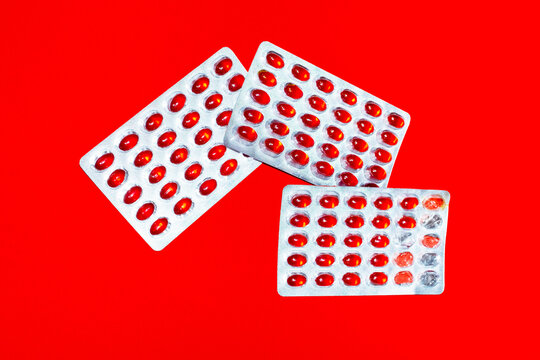 Red omega supplement capsule in a blister pack lies on red background