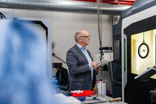 Male manager inspects machinery with a tablet in the production hall