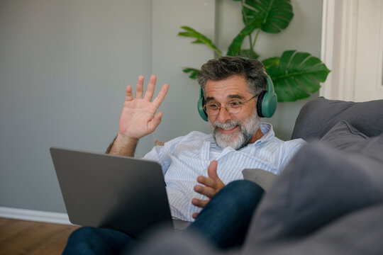 Smiling man wearing headphones using laptop for video call on couch