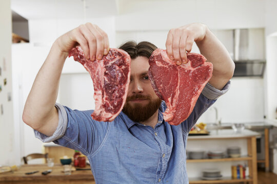 Man in kitchen holding two steaks