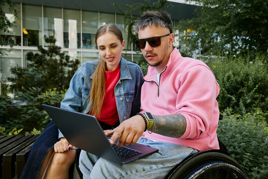 Man in a wheelchair and a woman discuss work on a laptop outdoors