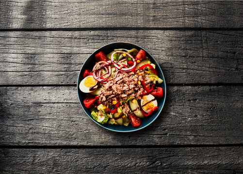 Fresh healthy tuna salad with egg and tomato sits on a wooden table
