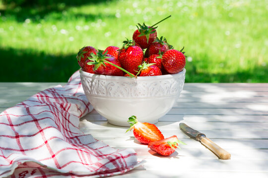Bowl of strawberries, knife and kitchen towel on garden table