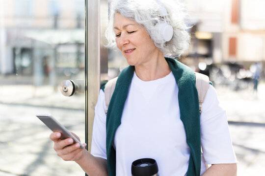 Woman waits at bus stop listening to music on smartphone