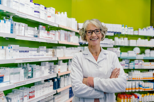 Portrait of smiling pharmacist at shelf with medicine in pharmacy