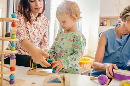 Little girl and teacher playing with toys in kindergarten