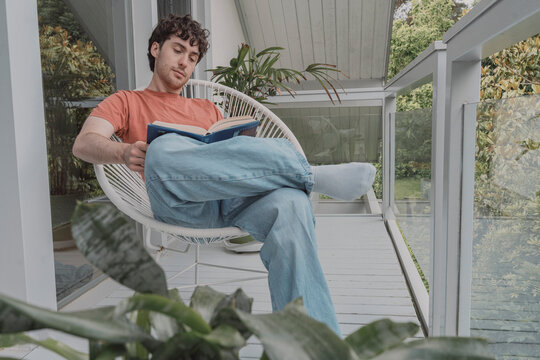 A young man reads a book on a balcony chair