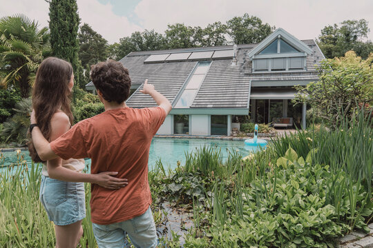 Couple stands in garden pointing at house roof with solar panel