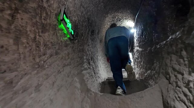 First-person view following a woman walking up narrow stone staircases in the dark, ancient tunnel of a cave city in Vardzia in Georgia, revealing hand-carved walls and a historic passageway