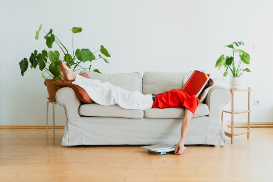 Tired woman covers her face with a book on the sofa