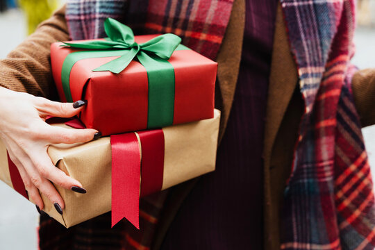 A woman holds two wrapped Christmas gifts outdoors during winter