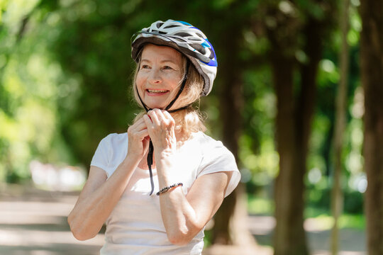 Smiling woman adjusts her bicycle helmet outdoors in the park