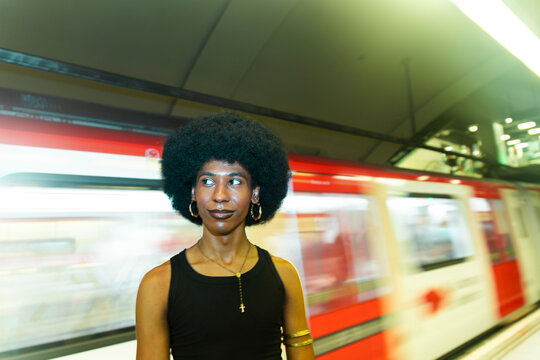 Stylish gender fluid person on subway platform with moving train