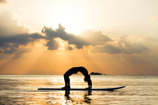 Thailand, man doing yoga on paddleboard at sunset, bridge position