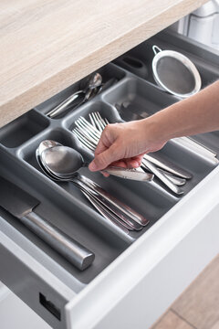 Hand picking up a spoon from an organized kitchen drawer