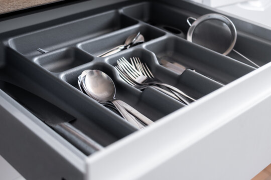 Close-up view of a neatly arranged cutlery drawer with spoons, forks, knives and kitchen utensils stored in a dark organizer tray in a modern home kitchen.