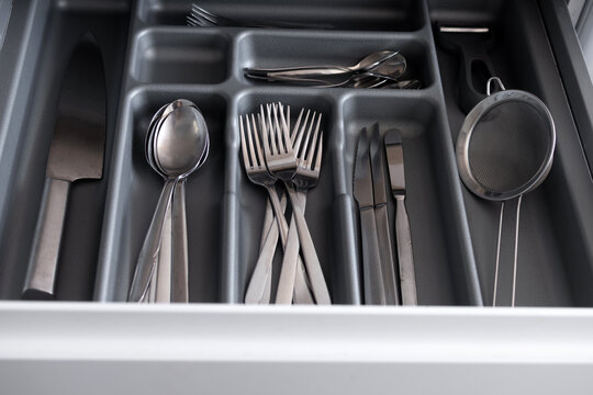Close-up view of a neatly arranged cutlery drawer with spoons, forks, knives and kitchen utensils stored in a dark organizer tray in a modern home kitchen.