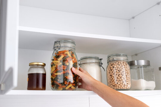 Hand taking a jar of colorful pasta from an organized kitchen pantry