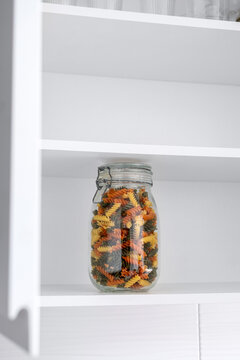 Glass jar filled with colorful pasta in kitchen cupboard