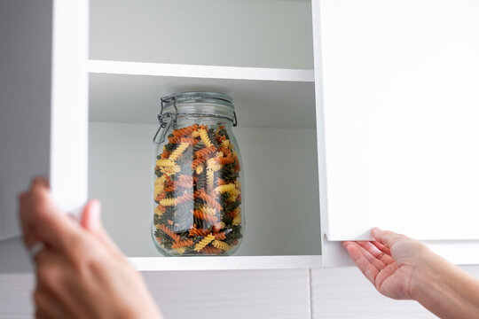 Person opening kitchen cupboard with jar of pasta inside