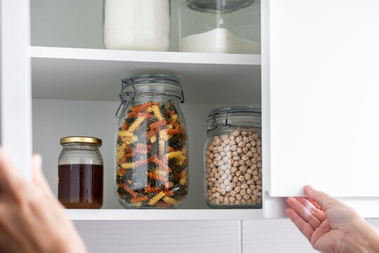 Person opening an organized kitchen pantry with dry food in glass jars