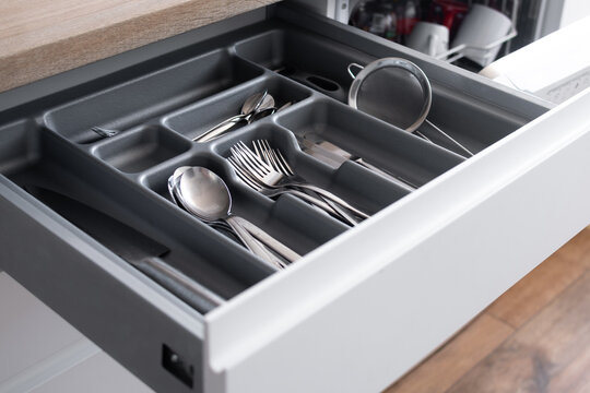 Close-up view of a neatly arranged cutlery drawer with spoons, forks, knives and kitchen utensils stored in a dark organizer tray in a modern home kitchen.
