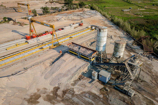 Aerial view of a concrete batching plant featuring a gantry crane, industrial silos, conveyor systems, and piles of raw materials in Semarang Regency, Central Java, Indonesia.