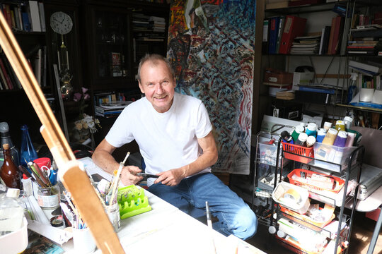 Smiling man holds paint brushes in his home art workshop