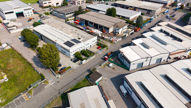 Aerial view of the industrial production district featuring warehouses with flat roofs, solar panels, paved roads, and parked vehicles in Milan, Lombardy, Italy.