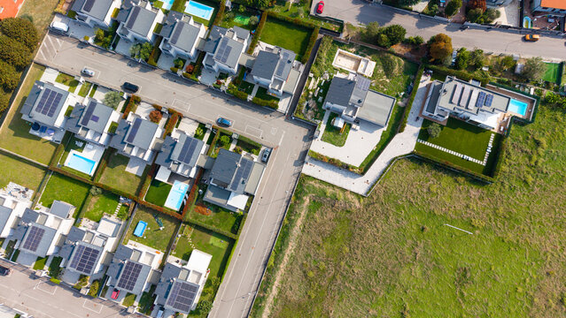 Aerial view of a modern gated villa community with private swimming pools, solar panels on rooftops, and manicured green lawns in Milan, Lombardy, Italy.