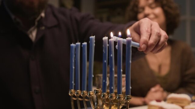 Caucasian man lighting blue Hanukkah menorah candles beside smiling woman. Footage perfect for Jewish holiday campaigns, winter festival advertisements, cultural family tradition projects