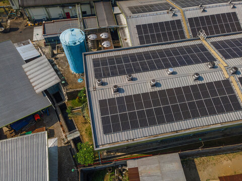 Aerial view of a factory roof covered with solar panels, featuring a prominent blue water tank and industrial ventilation units in Banyumas Regency, Central Java, Indonesia.