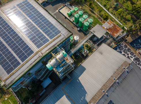 Aerial view of an industrial facility featuring solar panels on the roof, large green storage tanks, and metal roofing in Banyumas Regency, Central Java, Indonesia.