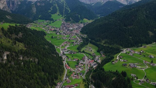 High angle aerial push over Selva di Val Gardena village and green alpine meadows on overcast day, Dolomites, South Tyrol, Alps, Italy