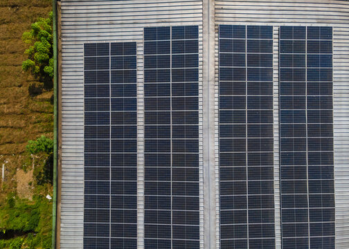 Aerial view of solar panels installed on a metal roof with adjacent green vegetation in Banyumas Regency, Central Java, Indonesia.