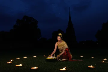 Thai Woman In Elegant Traditional Dress Holding A Krathong Basket Surrounded By Candlelight In An Ancient Temple Park At Night Celebrating Loy Krathong Festival In Thailand © SHUTTER DIN