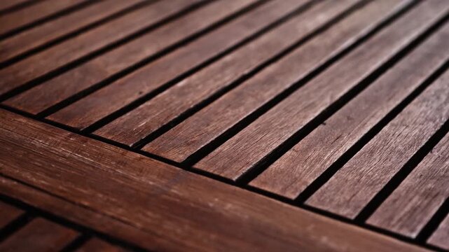 Close-up of a dark wooden slatted tabletop texture illuminated by soft natural sunlight.