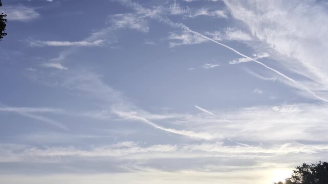 cielo azzurro solcato da scie di condensazione di aerei che si intrecciano tra nuvole leggere al mattino