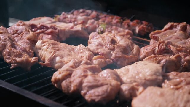 Close-up shot of juicy meat grilling on an outdoor barbecue grate with rising smoke on a sunny day.