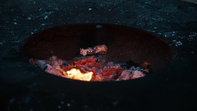 Close-up of bright orange flames burning wood inside a round outdoor fire pit.