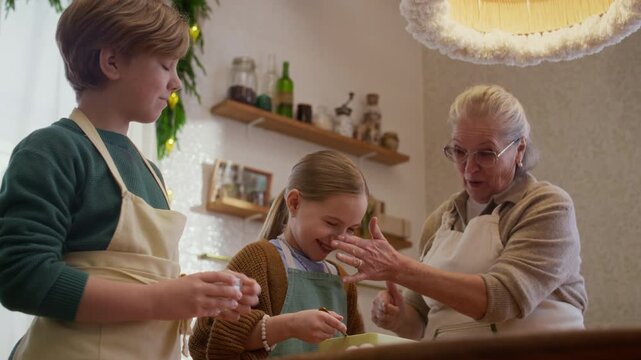 Senior Caucasian woman baking cookies and playing with grandchildren in kitchen. Ideal for family lifestyle advertising, baking product promotions, and intergenerational campaigns