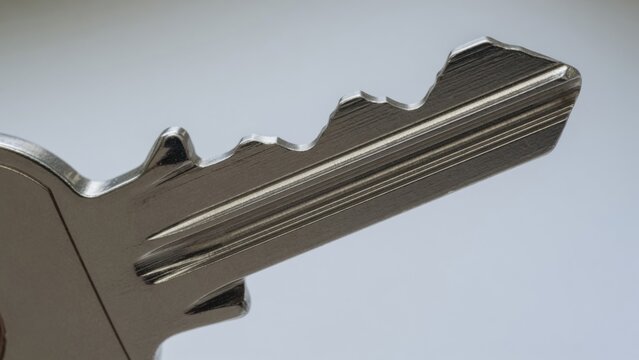 metallic key in neutral setting with silver and gray tones close-up perspective security services home security locksmith services editorial visual resource design story.