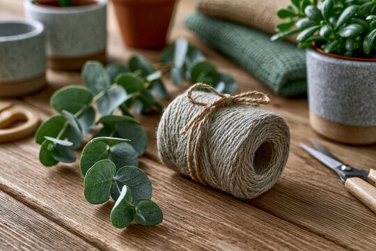 Elegant flat lay of diy home decor materials including twine, eucalyptus stems, ceramic pots, scissors and natural fabrics on a wooden surface, bright diffused lighting