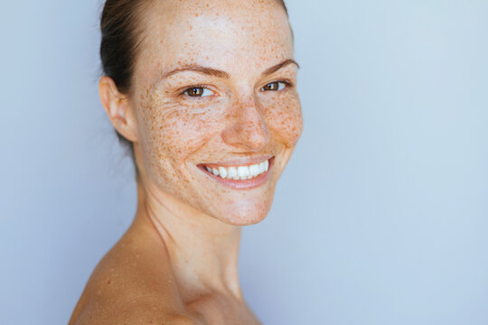 Beauty skincare portrait made with a natural light, of a woman with a clean nourished skin and freckles posing against light backgorund