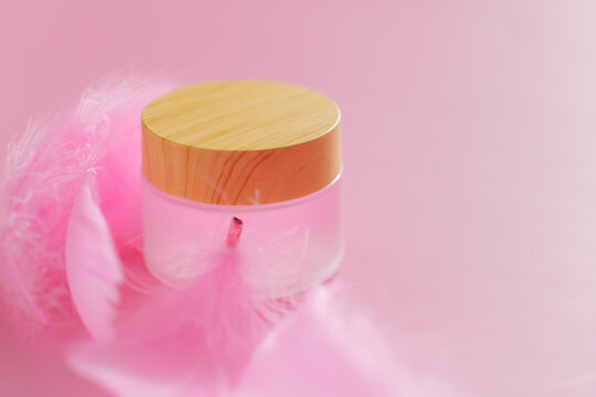  Cosmetic jar with pink feathers in soft focus for product mockups, branding, natural cosmetics, and wellness concepts.