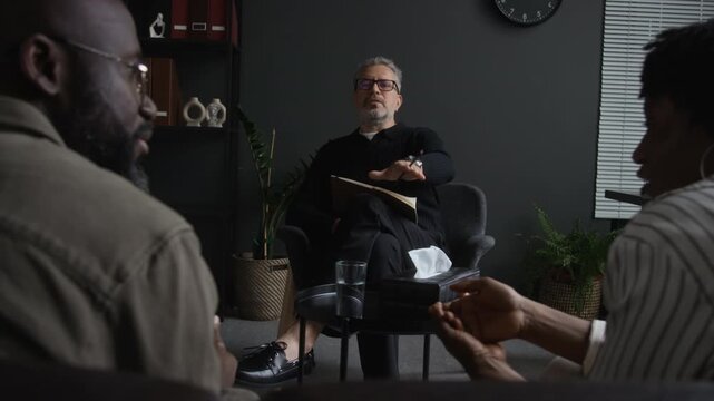 Middle aged Caucasian psychologist calming arguing African American couple during counseling session. Footage suitable for mental health commercials and marriage therapy campaigns