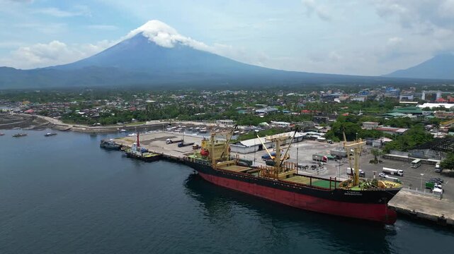 Cinematic aerial footage of a large cargo ship navigating the waters near Tabaco City, Albay, Philippines, with Mayon Volcano visible in the background. Clear sunny weather and blue skies highlight th