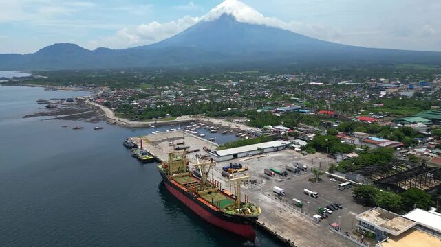 Aerial view of a large commercial freighter near Tabaco Port in Albay, Philippines, with the perfectly shaped Mayon Volcano visible behind the vessel. Cinematic maritime transportation scene captured